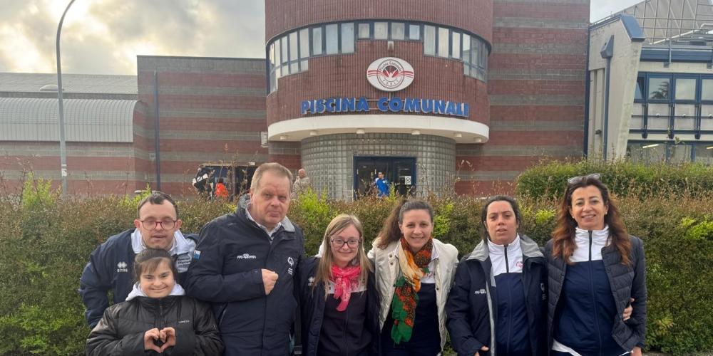 Gruppo sorridente davanti a una piscina comunale, sprigionano gioia e unità.