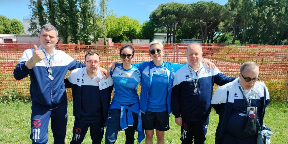 Gruppo felice di atleti con medaglie, sorrisi e un pollice in su.